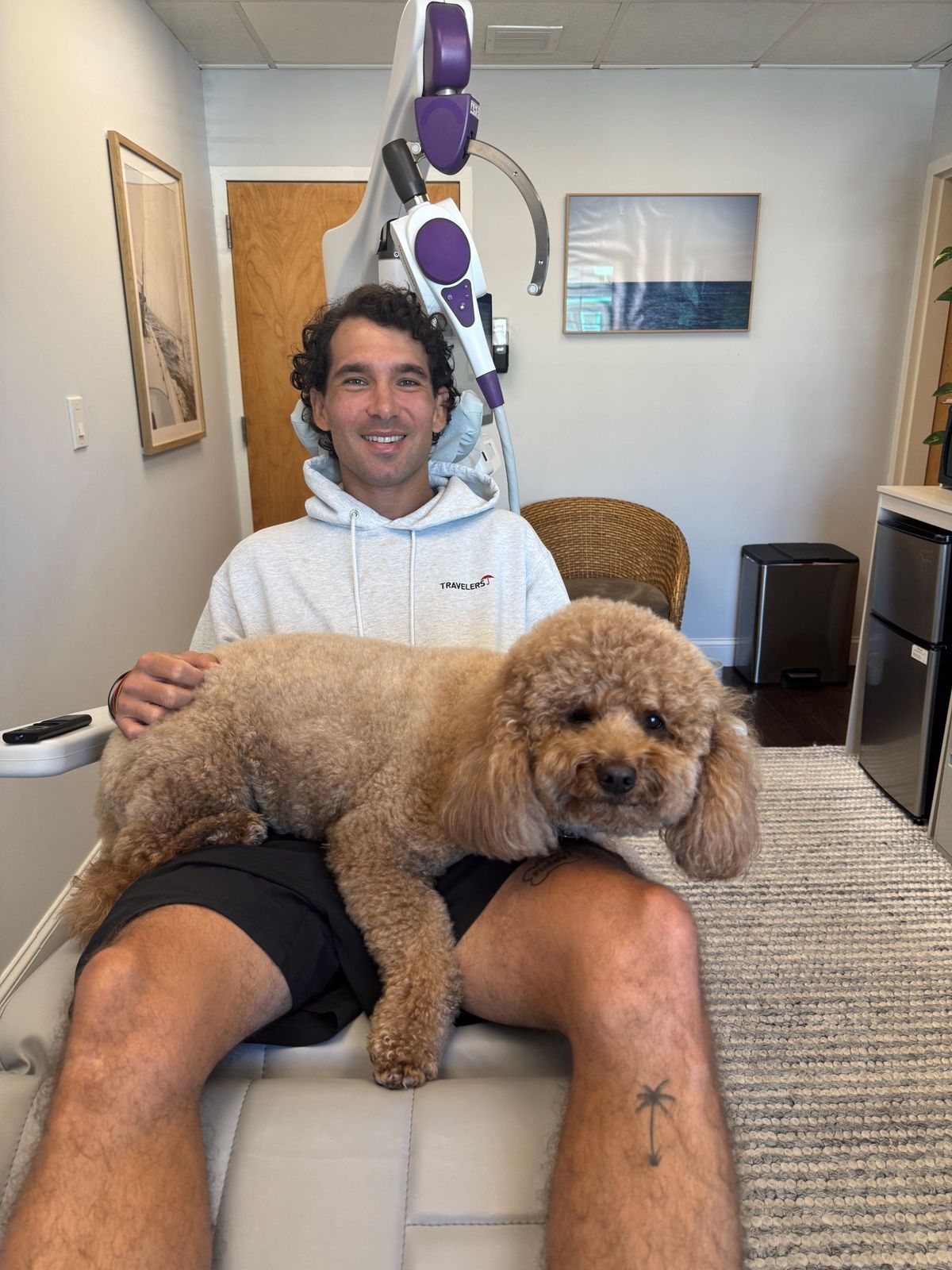 A smiling patient seated in the NeuroStar treatment chair with a therapy dog resting on his lap